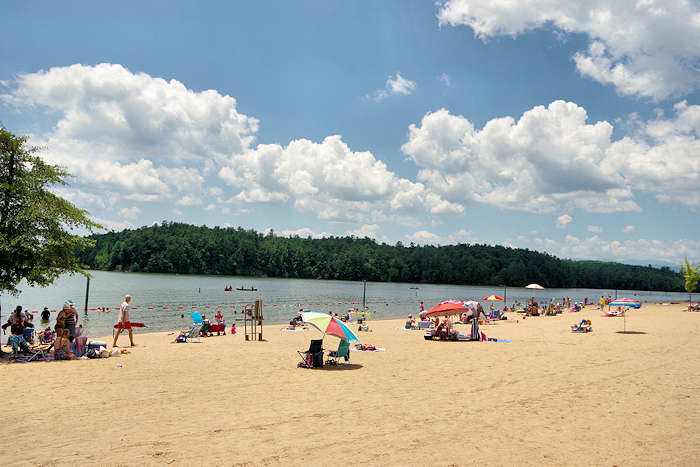 Beach with people, umbrellas, trees, sand, and clouds. Lake James in North Carolina