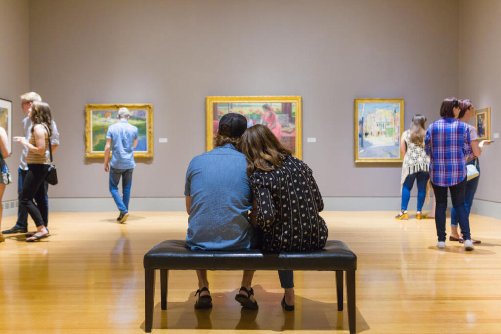 a couple sitting on a bench in an art museum surround by art and other people