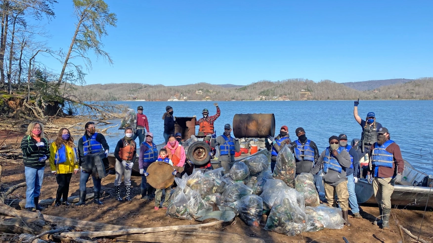 People standing in front of river with trash bags