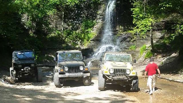 jeeps on a trail in front of a waterfall, man in a red shirt