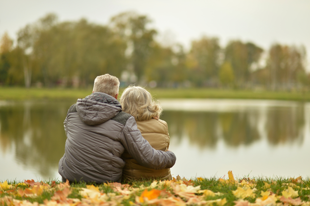 Man with arm around woman---both wearing jackets and looking at the water together. 
