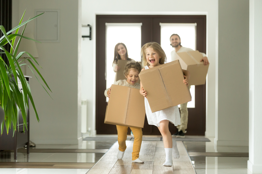 Children running with boxes into new house with parents in the background also holding boxes