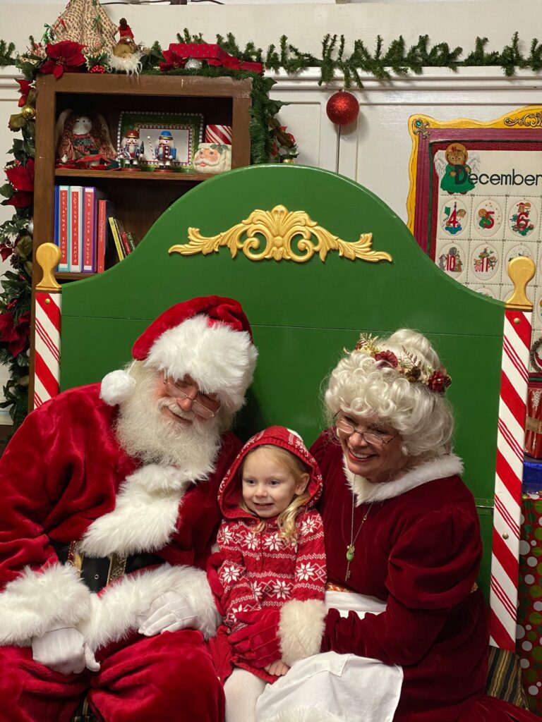 Santa and Mrs. Clause posing with a child for a picture. 