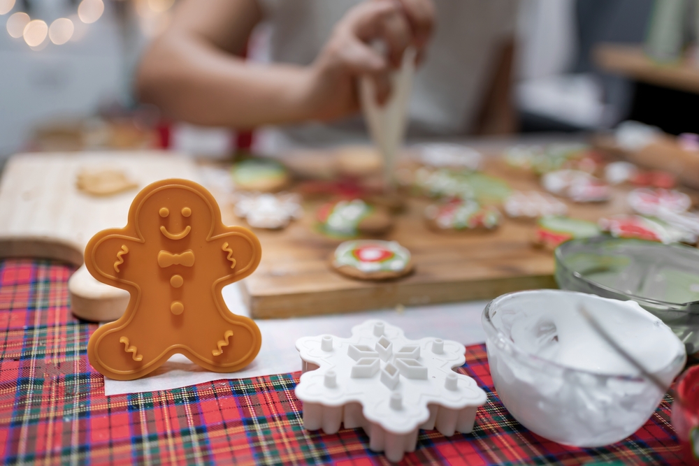 Gingerbread man in front of blurred Christmas cookies being decorated. 