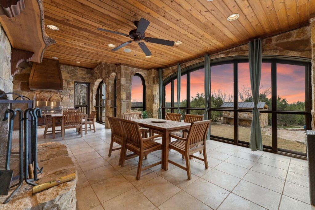 outdoor room with a table, windows, fireplace, and kitchenette