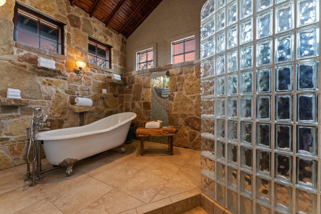 a clawfoot bathtub in a stone room and frosted glass