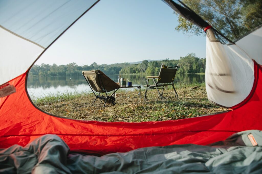 Interior of a camping tent with chairs outside next to a lake