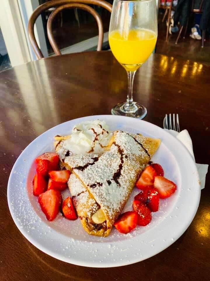 A crepe covered in powdered sugar, strawberries, and chocolate syrup with a mimosa. 