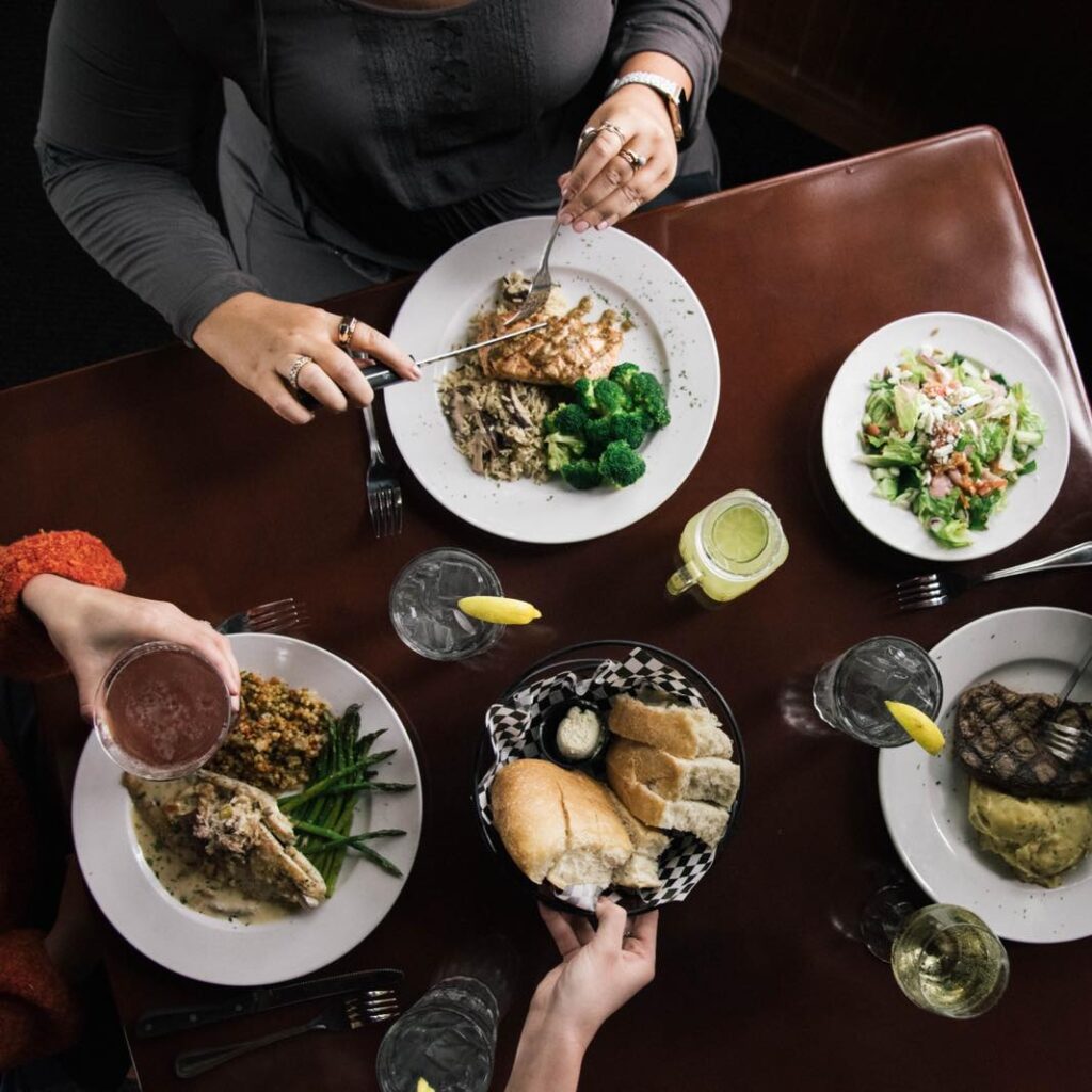 Four dishes of food---two types of chicken, a salad, and steak---at a table with bread in the middle. 