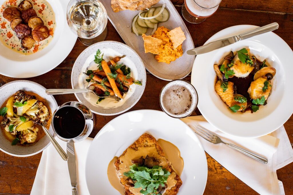 Various white plates with fresh food on them including fish, vegetables, scallops, and more. 