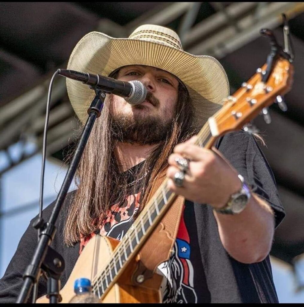 A singer with a guitar, cowboy hat, and long hair