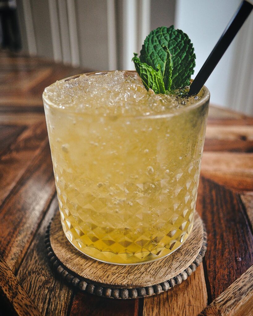 Yellow cocktail in glass garnished with mint