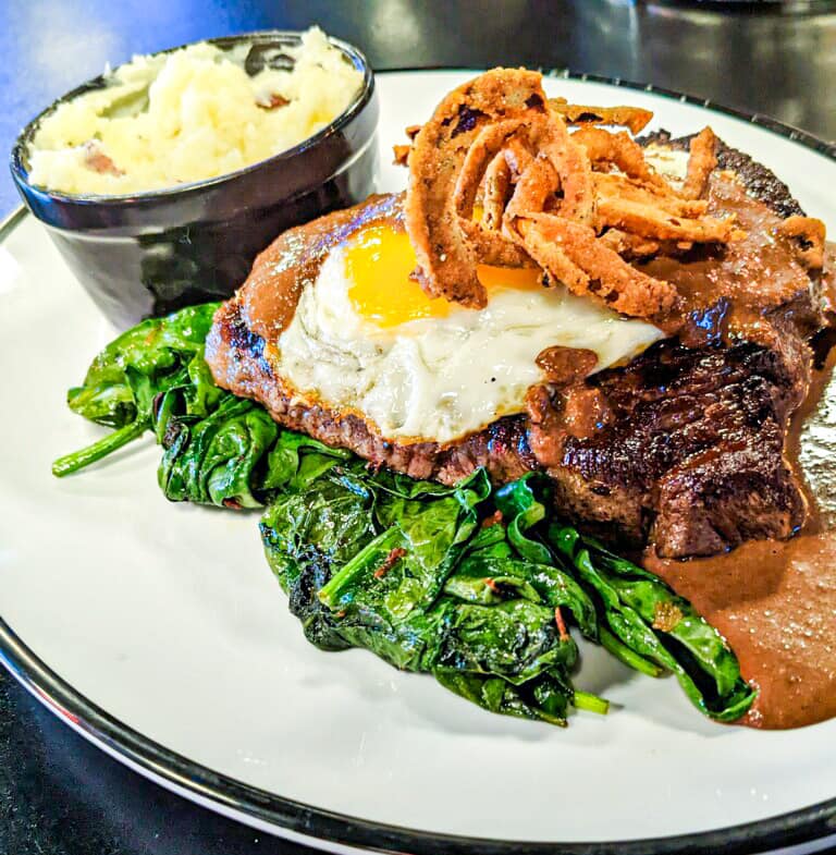 Sirloin steak with spinach, onion rings, and a fried egg.