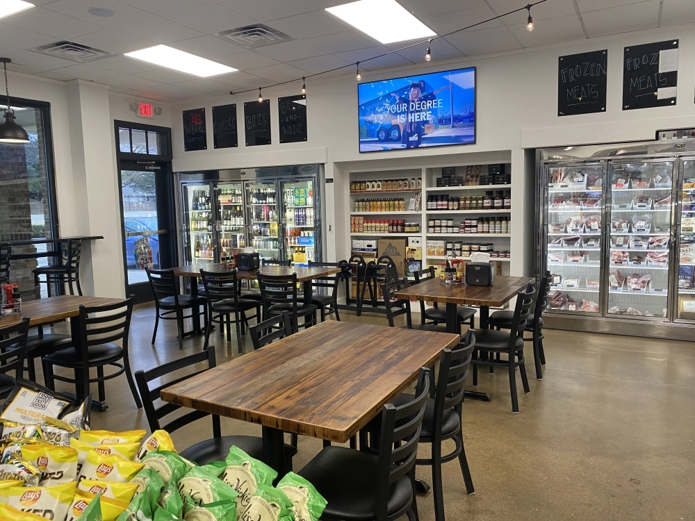 Wooden tables with black chairs in front of refrigerated items.