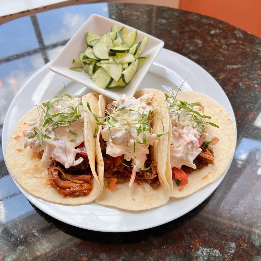 Tacos with sauce and garnish beside a bowl of cucumbers.