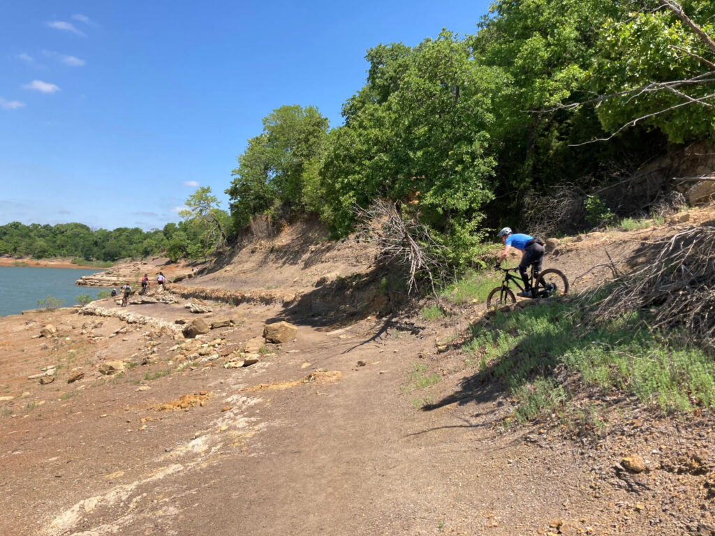 Biker riding on the North Shore trail with some hikers in the distance near Lake Grapevine, TX.