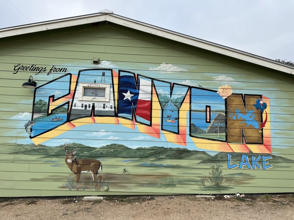 The Words "Greetings from Canyon Lake" on the side of a building. A paining of a deer is featured.