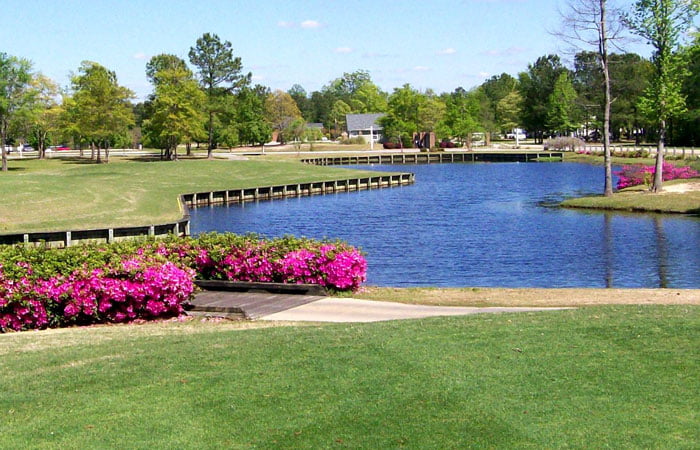 The Players Course at Wyboo, showcasing pink flowers, a small lake, green trees, and gently rolling hills.